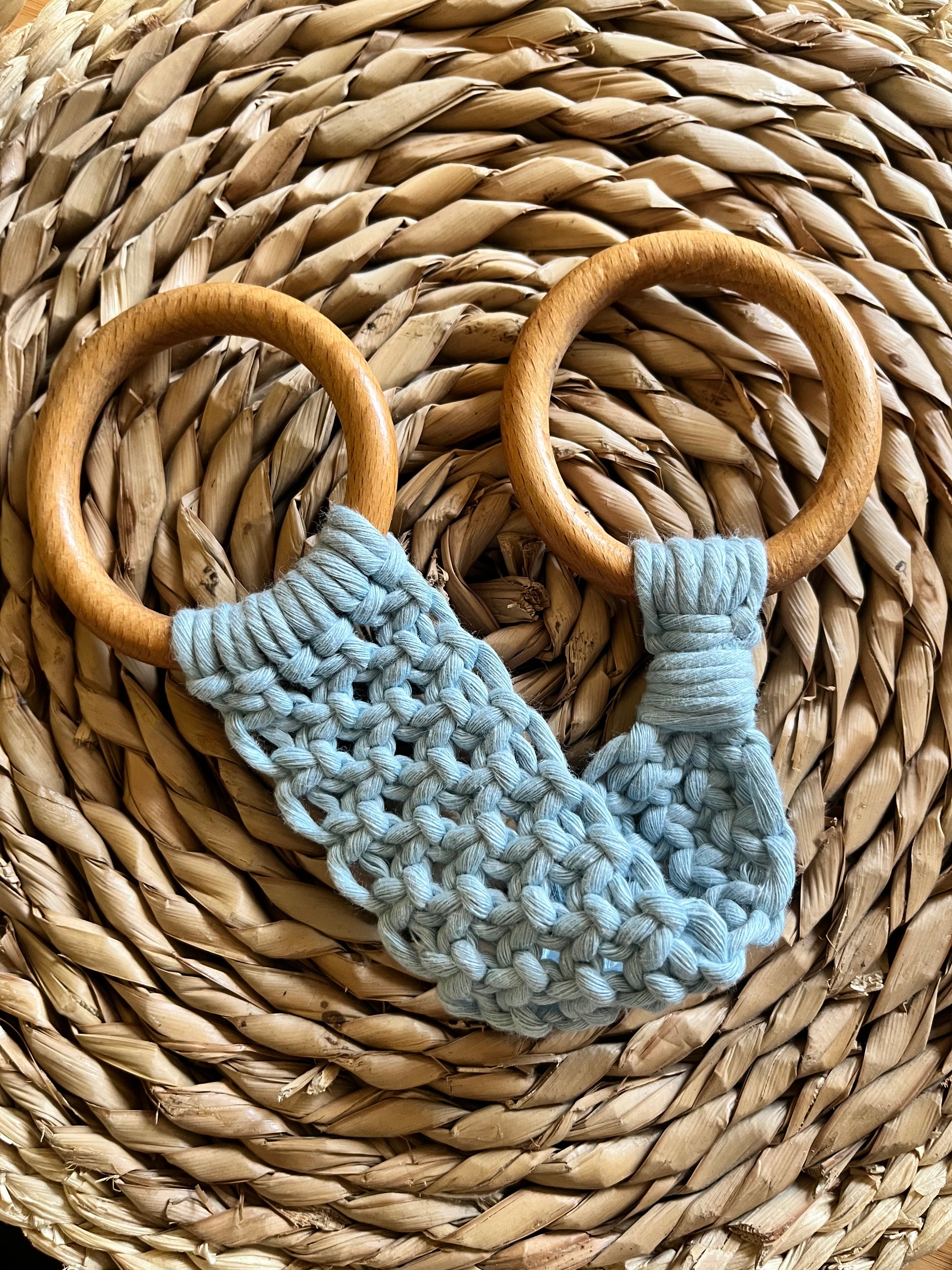 A blue macrame towel ring holder made with intricate knots and two smooth, wooden rings is laid on a woven, circular mat.