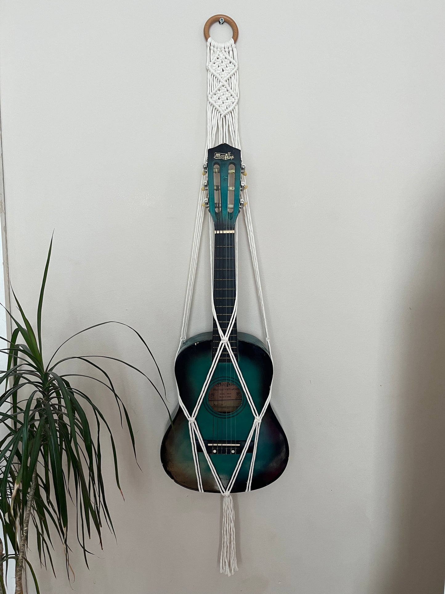 Blue guitar securely held in a macrame instrument hanger on a light background
