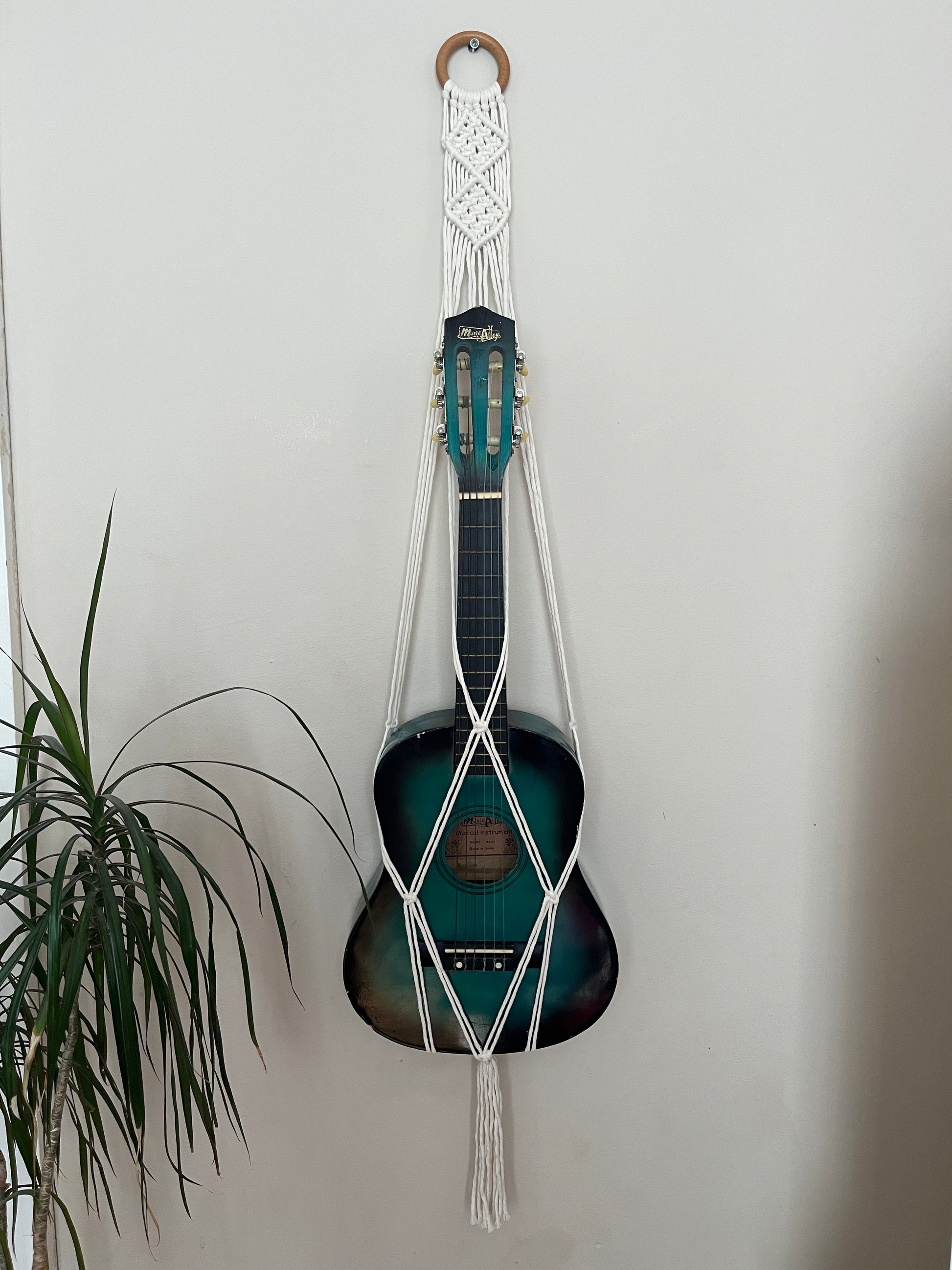 Blue guitar securely held in a macrame instrument hanger on a light background