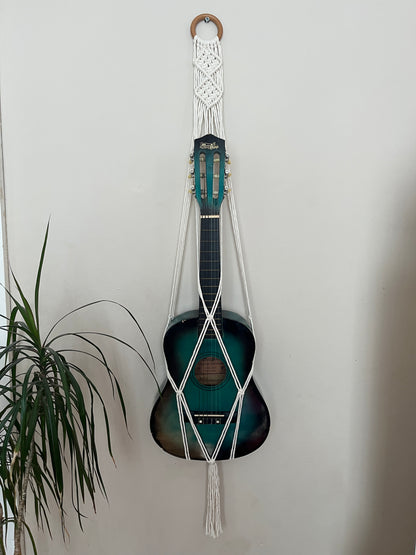 Blue guitar securely held in a macrame instrument hanger on a light background