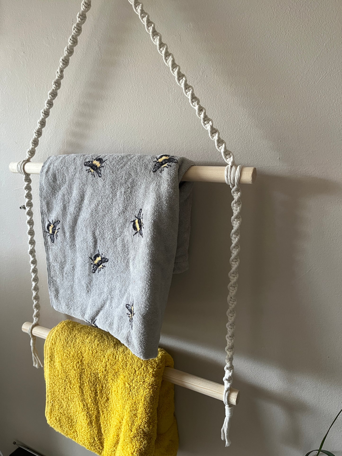 Close up of two towels hanging on a macrame towel rail against a beige wall 