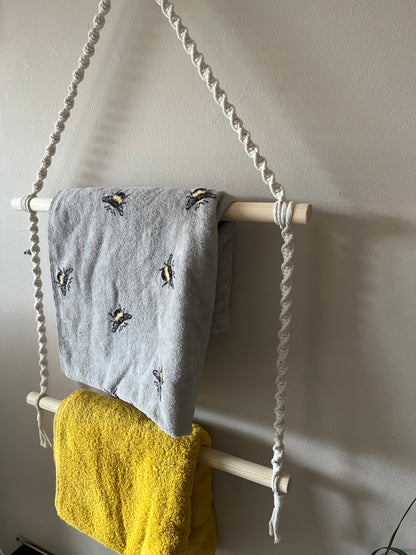 Close up of two towels hanging on a macrame towel rail against a beige wall 