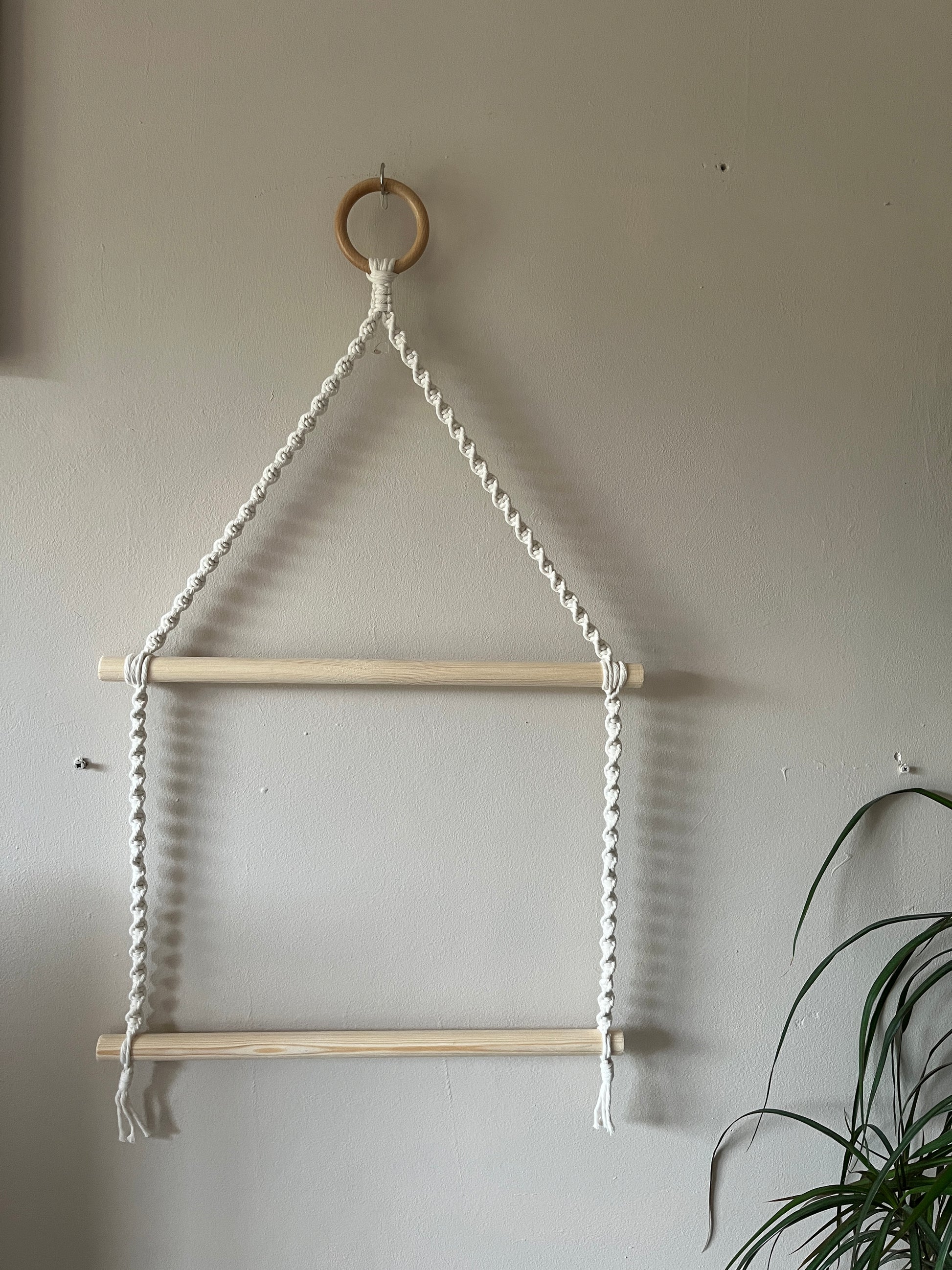 Macrame towel ladder hanging against a beige wall with a plant in the corner