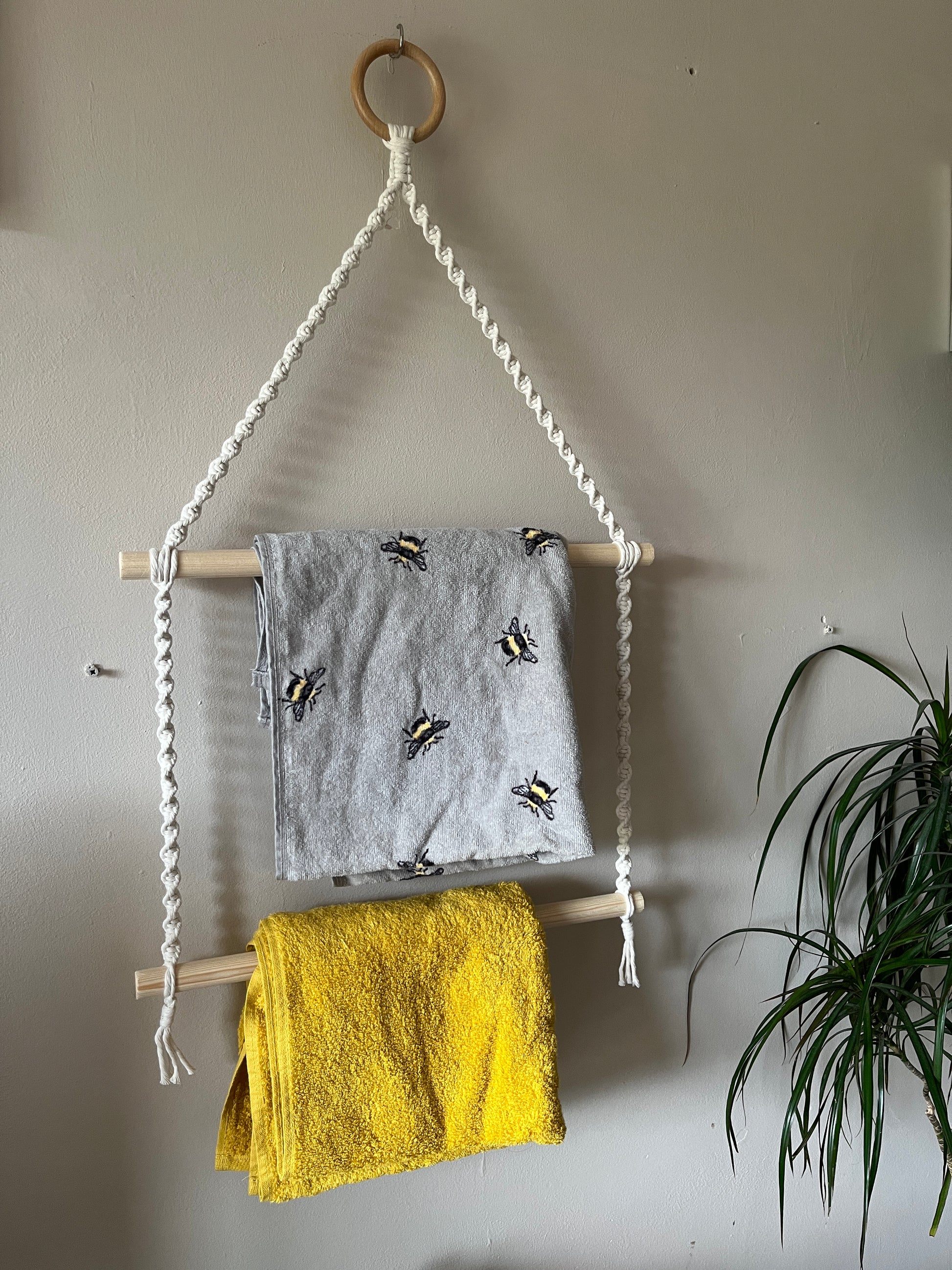 Hanging towel rail holding a grey and a yellow towel against a beige wall.