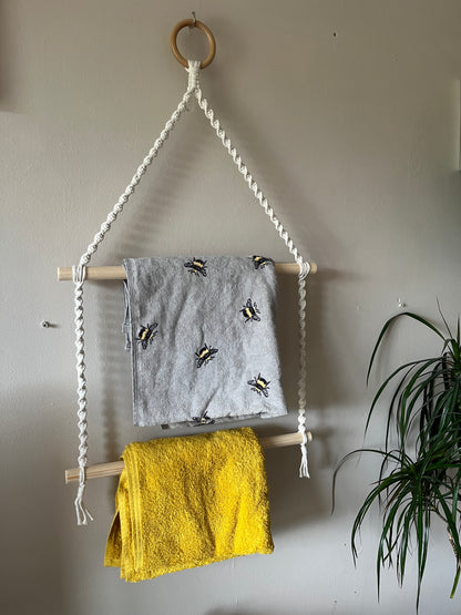 Hanging towel rail holding a grey and a yellow towel against a beige wall.