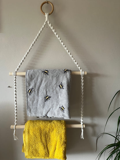 Towels hanging on a rack against a white wall with a plant in the corner.