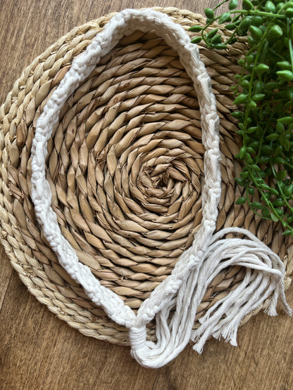 A handmade boho style macrame hat band with a long tassel, made with recycled cotton, and an intricate knot pattern. 