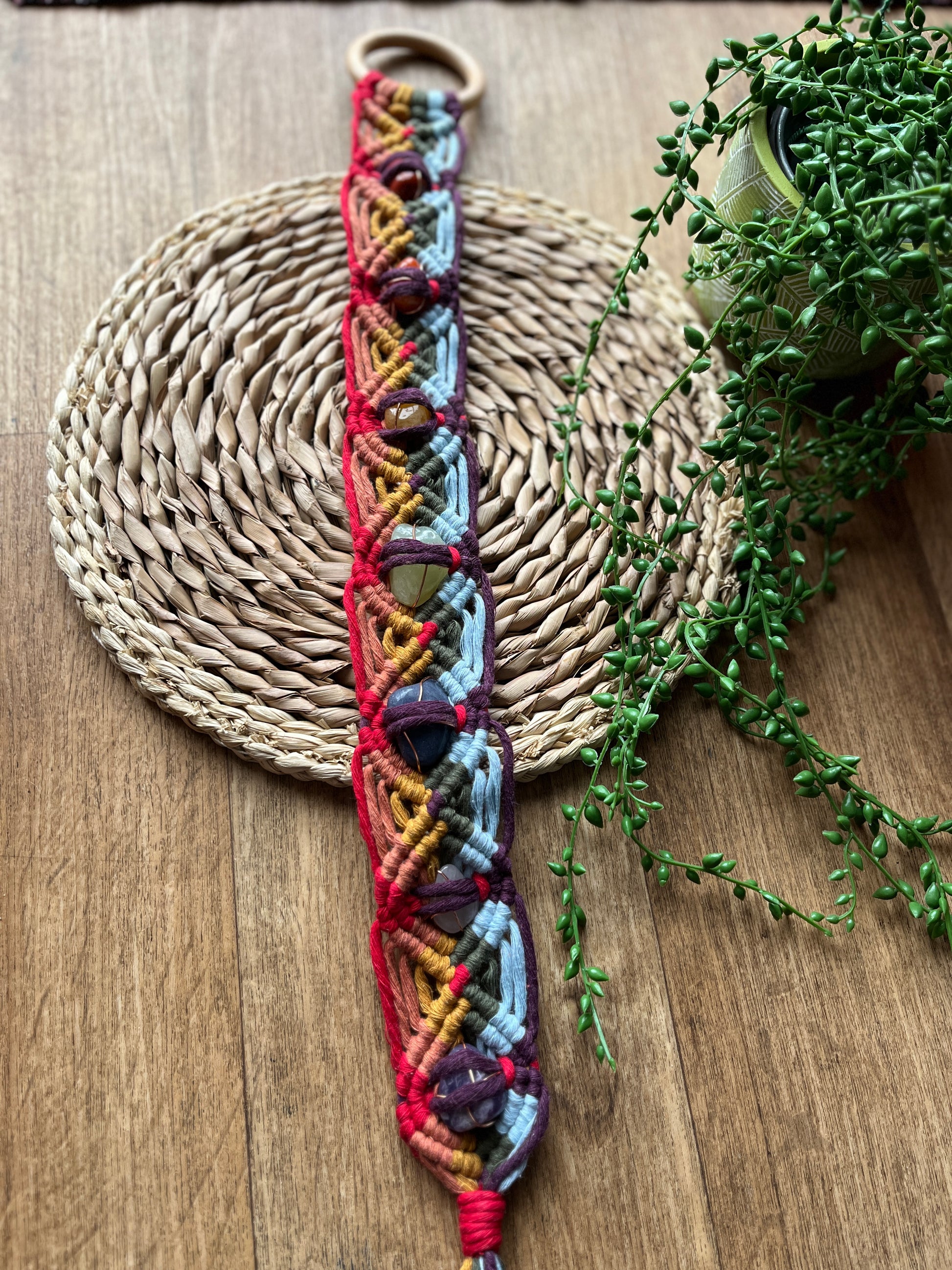 Colourful macrame chakra gemstone wall hanging on a woven mat with greenery