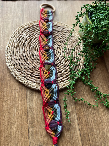 Colourful macrame chakra gemstone wall hanging on a woven mat with greenery
