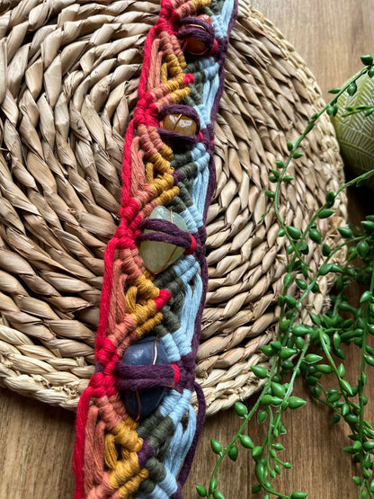 Close up of a colourful macrame chakra gemstone wall hanging on a woven mat with greenery