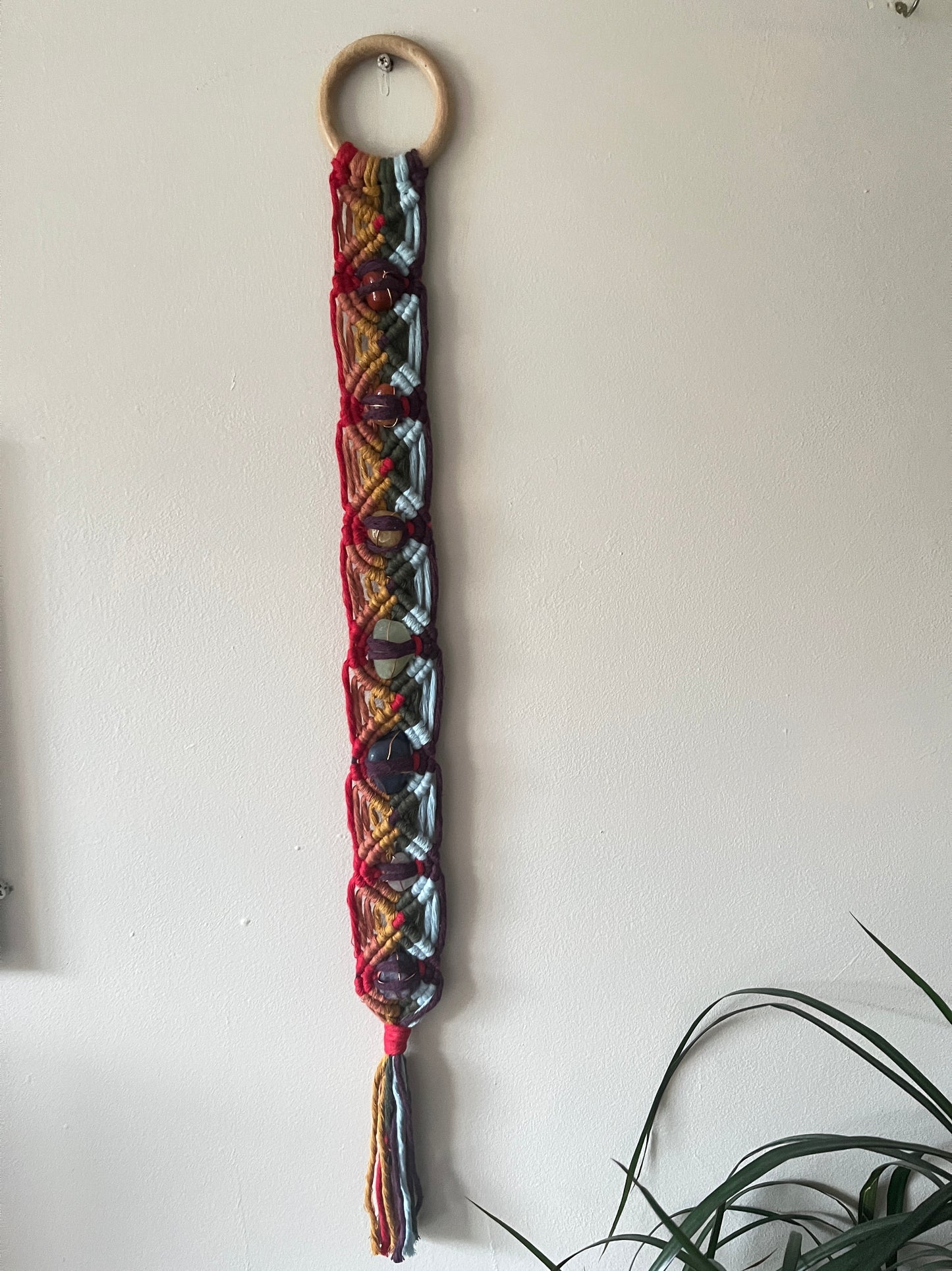 Colourful macrame chakra gemstone wall hanging on a beige wall 