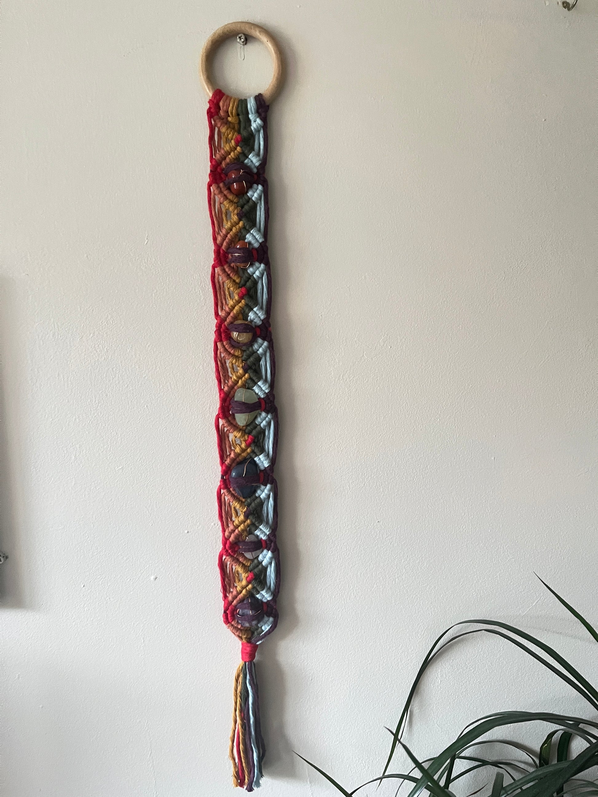 Colourful macrame chakra gemstone wall hanging on a beige wall 