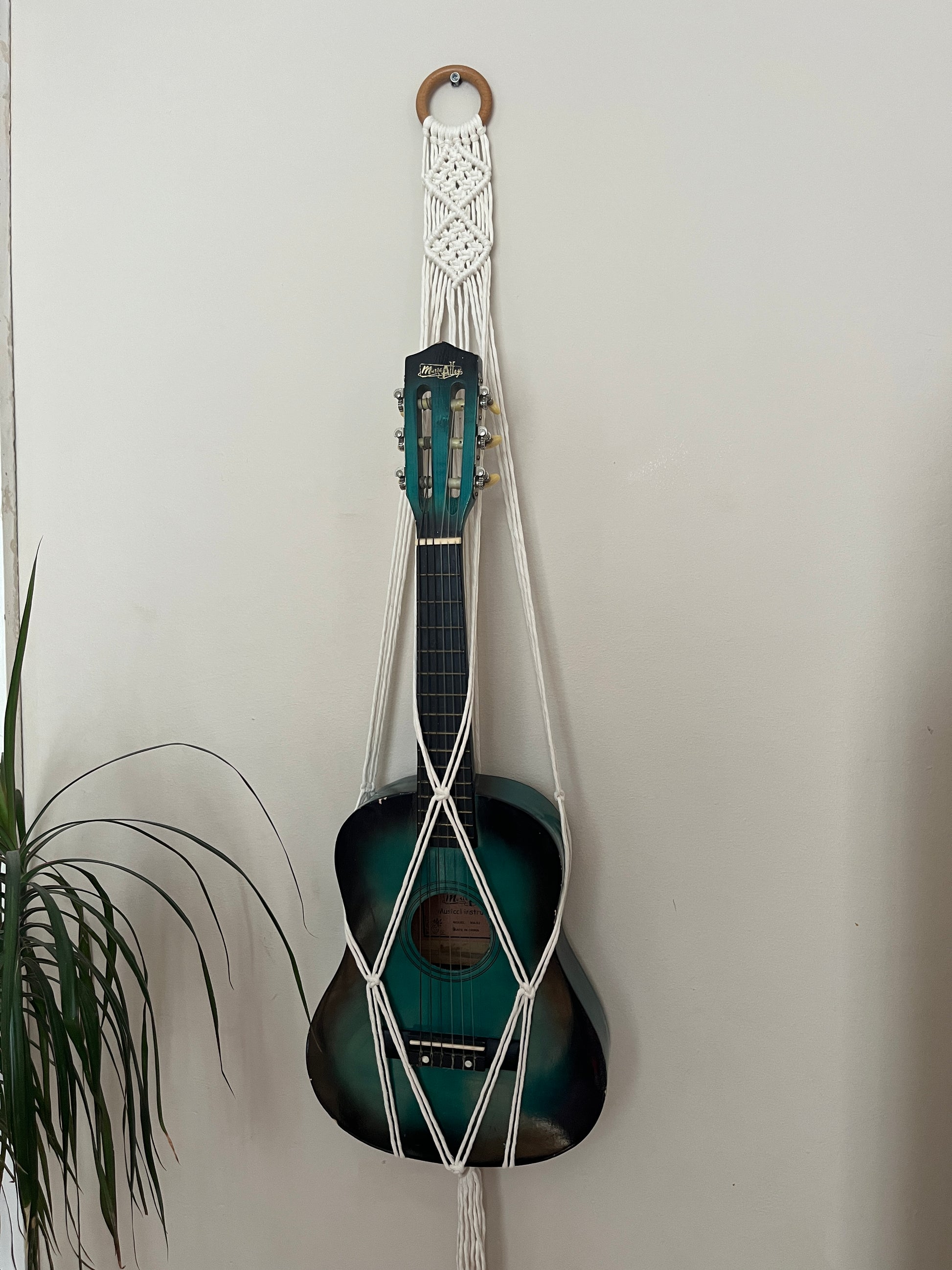 Blue 1/4 guitar securely held in a macrame instrument hanger on a light background
