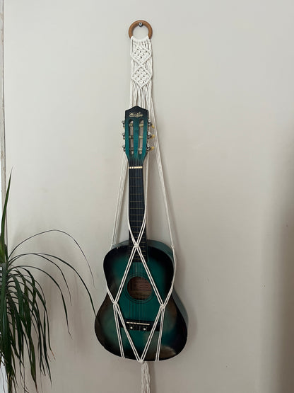 Blue 1/4 guitar securely held in a macrame instrument hanger on a light background