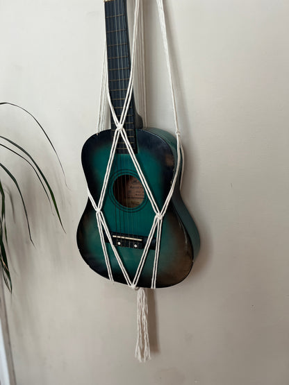Close up of the body of a blue 1/4 guitar securely held in a macrame instrument hanger on a light background