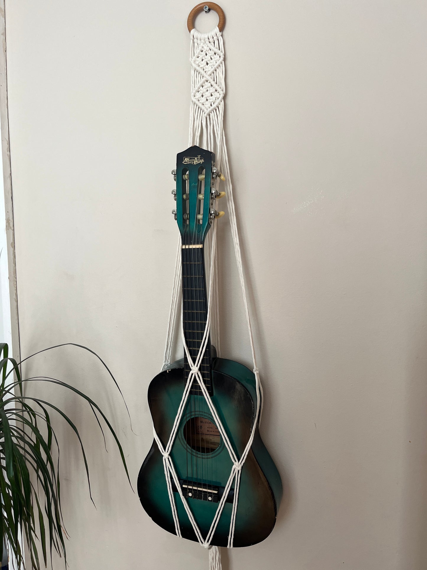 Blue guitar securely held in a macrame instrument hanger on a light background