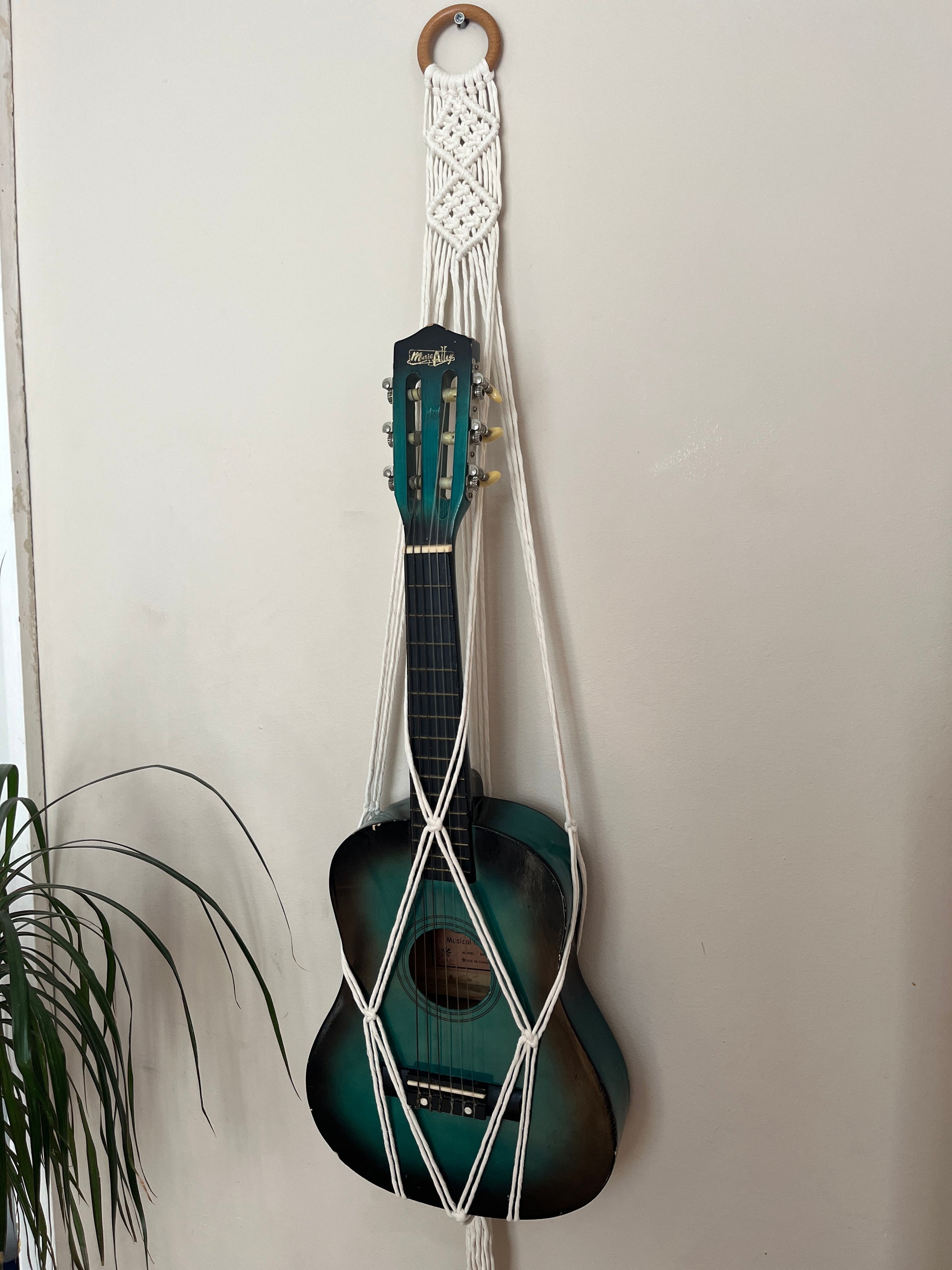 Blue guitar securely held in a macrame instrument hanger on a light background
