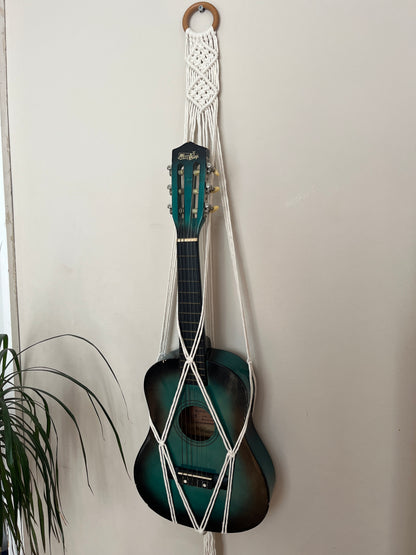 Blue guitar securely held in a macrame instrument hanger on a light background