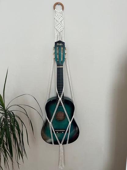 Blue 1/4 size child's guitar securely held in a macrame instrument hanger on a light background