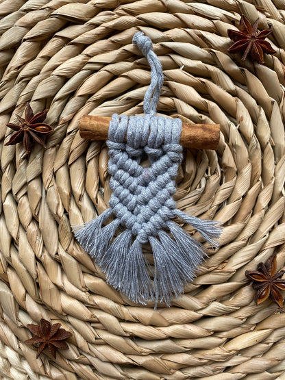 A handmade macrame christmas tree decoration made with recycled cotton and a real cinnamon stick, laid out on a round wicker mat surrounded by star anise for decoration.