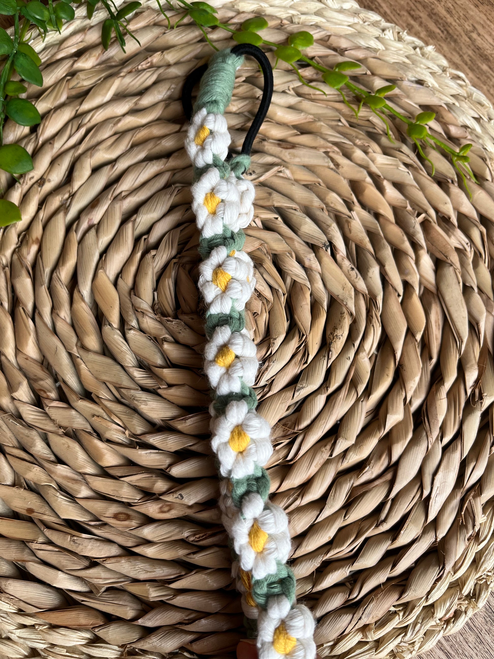 A macrame daisy chain headband made with white yellow and green cotton, laid neatly on a woven placemat. 