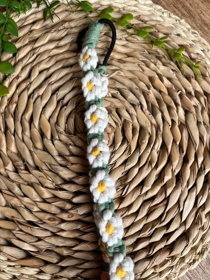 A macrame daisy chain headband made with white yellow and green cotton, laid neatly on a woven placemat. 