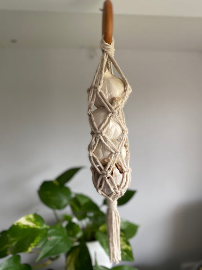 A handmade macrame garlic hanger made with natural cotton yarn and a wooden ring, with 4 fresh garlic bulbs inside.