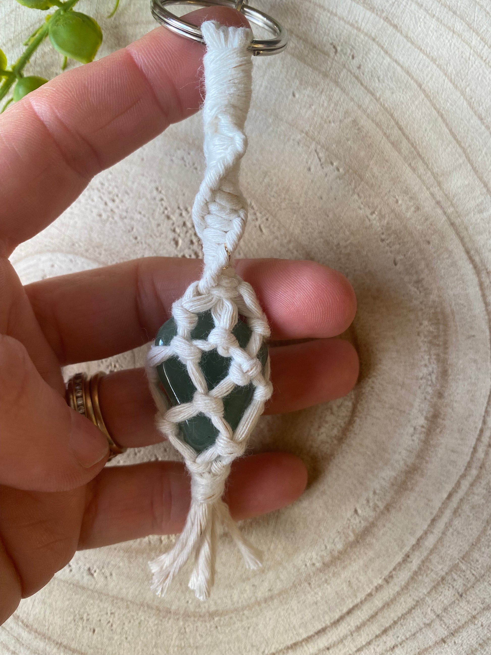 A hand holding a handmade macrame gemstone keyring, made with natural coloured cotton yarn wrapped around a green quartz  gemstone.