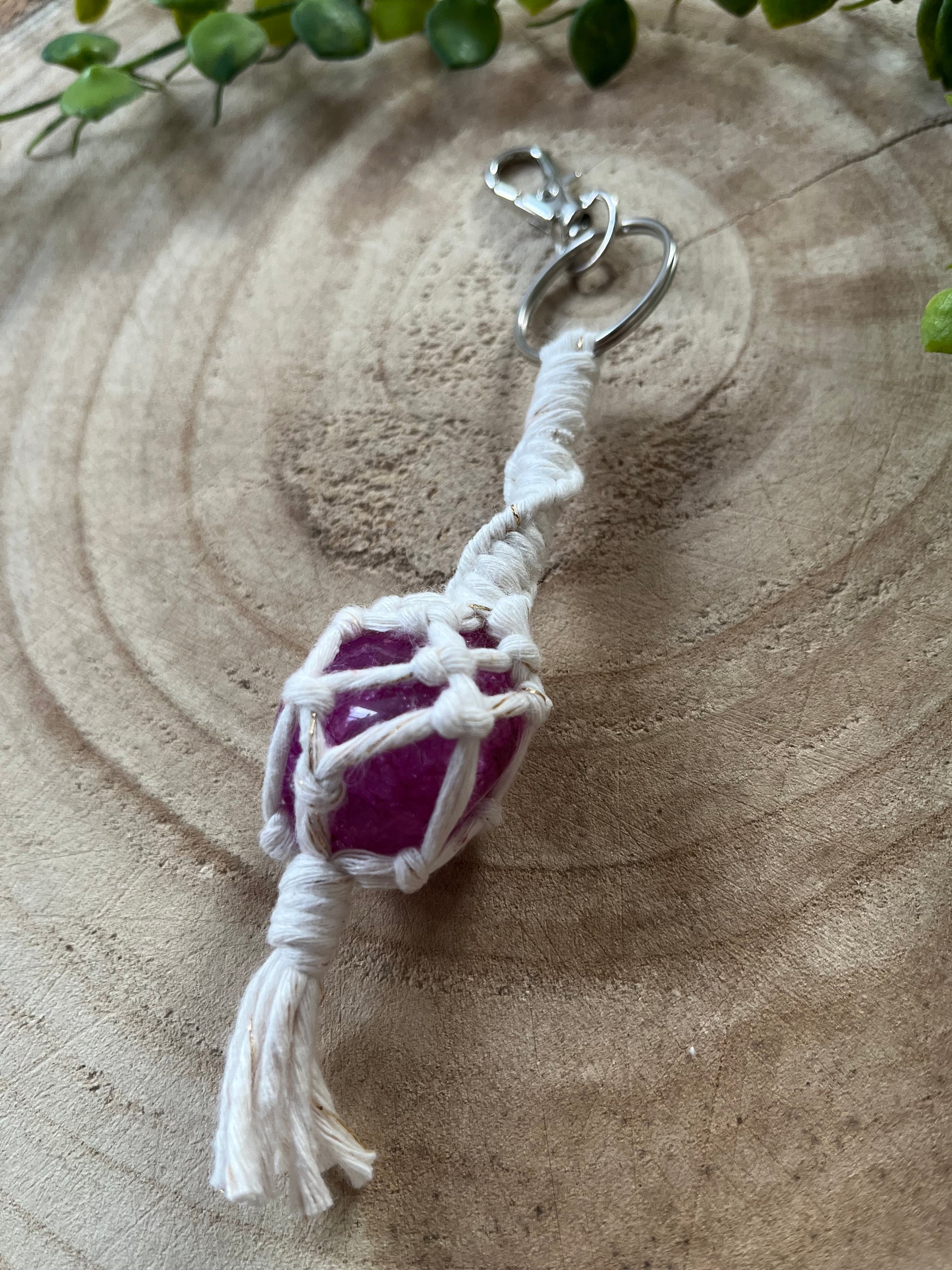 A handmade macrame gemstone keyring, made with natural coloured cotton yarn wrapped around a pink crackle quartz gemstone, and metal split ring clasp, on a wooden surface.