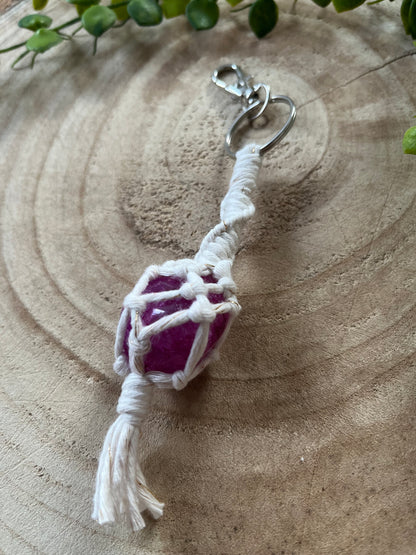 A handmade macrame gemstone keyring, made with natural coloured cotton yarn wrapped around a pink crackle quartz gemstone, and metal split ring clasp, on a wooden surface.