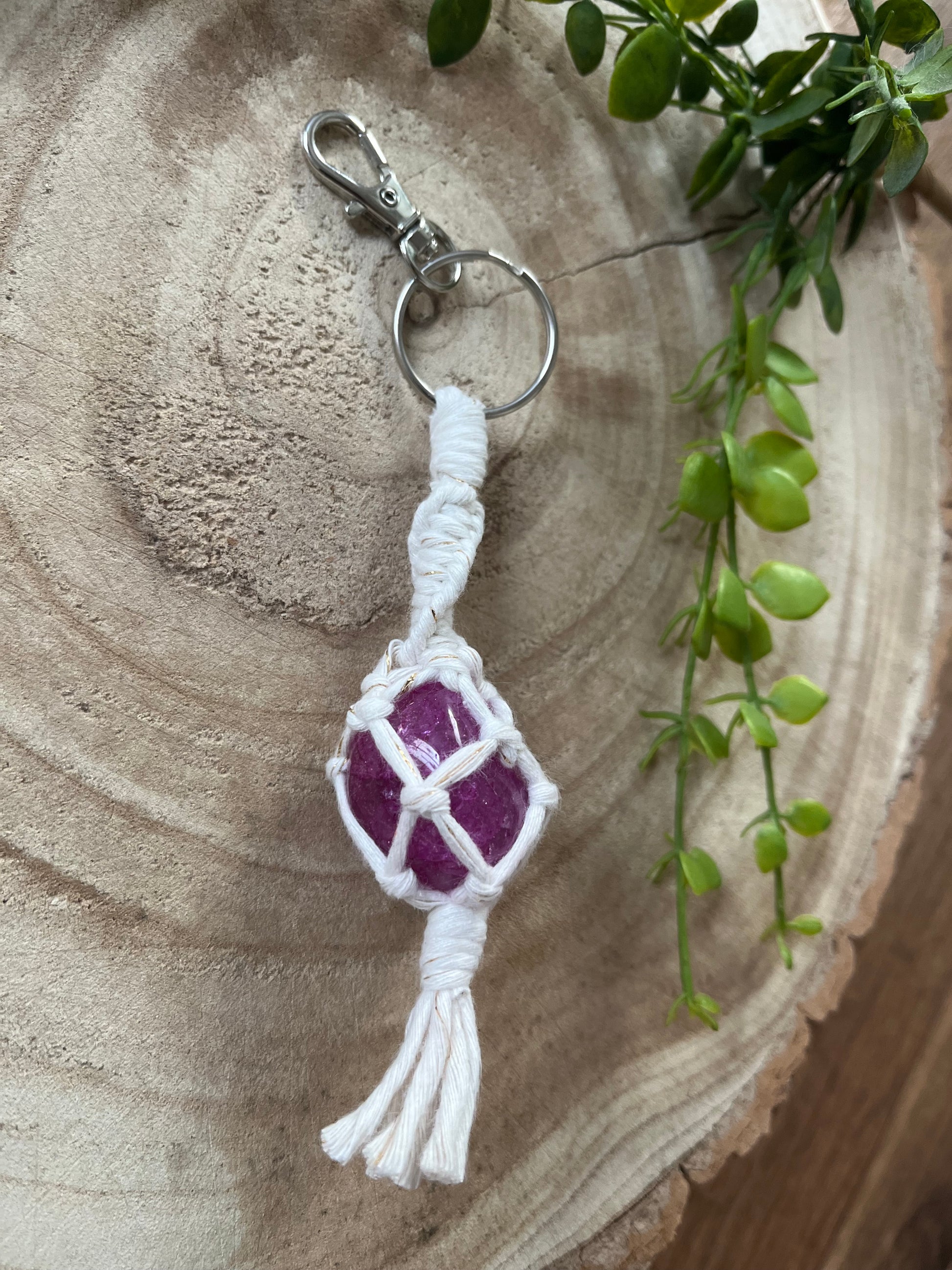 Close up of a handmade macrame gemstone keyring, made with natural coloured cotton yarn wrapped around a pink crackle quartz gemstone, and metal split ring clasp, on a wooden surface.