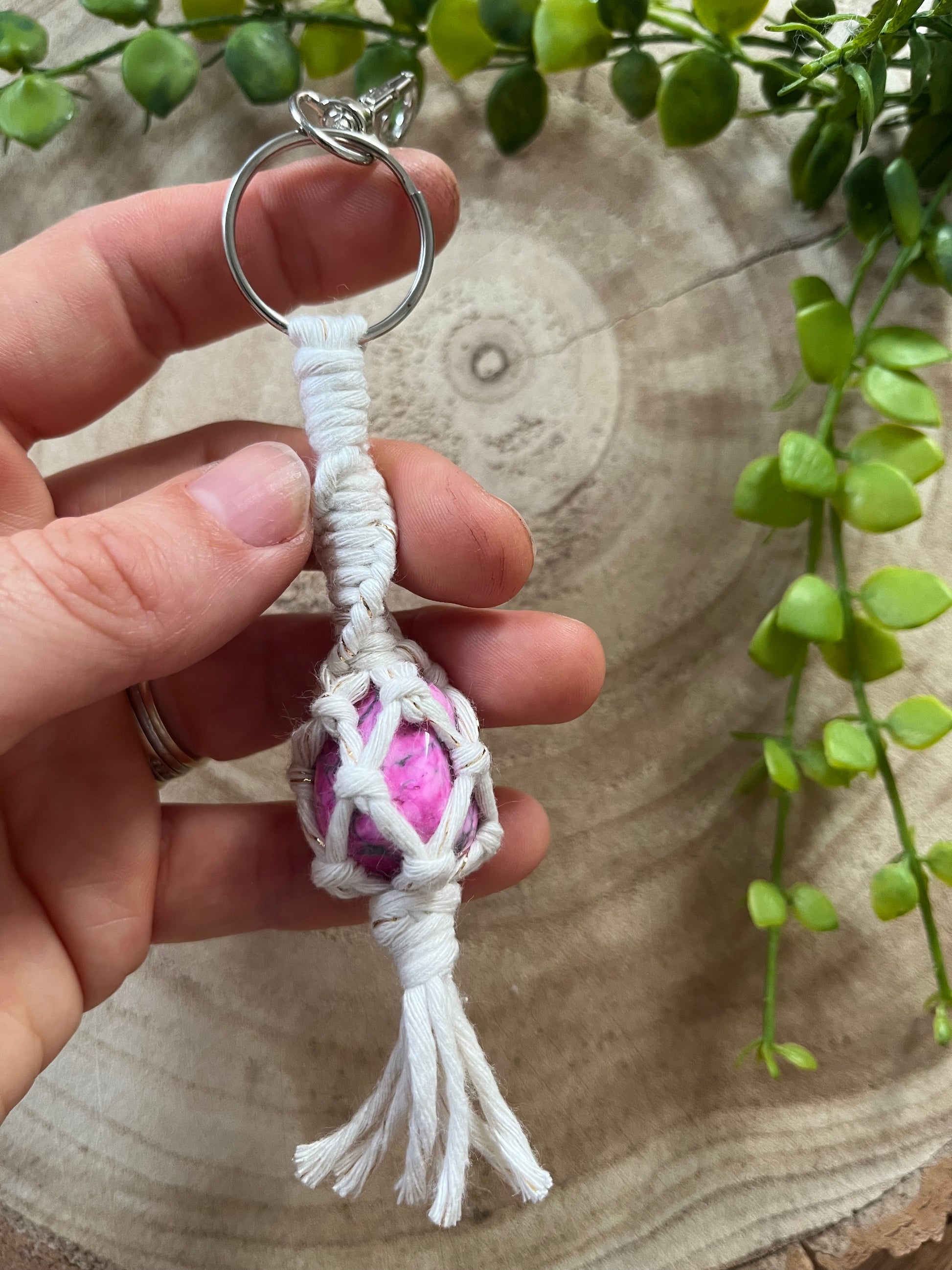 A hand holding a handmade macrame gemstone keyring, made with natural coloured cotton yarn wrapped around a pink howlite gemstone.