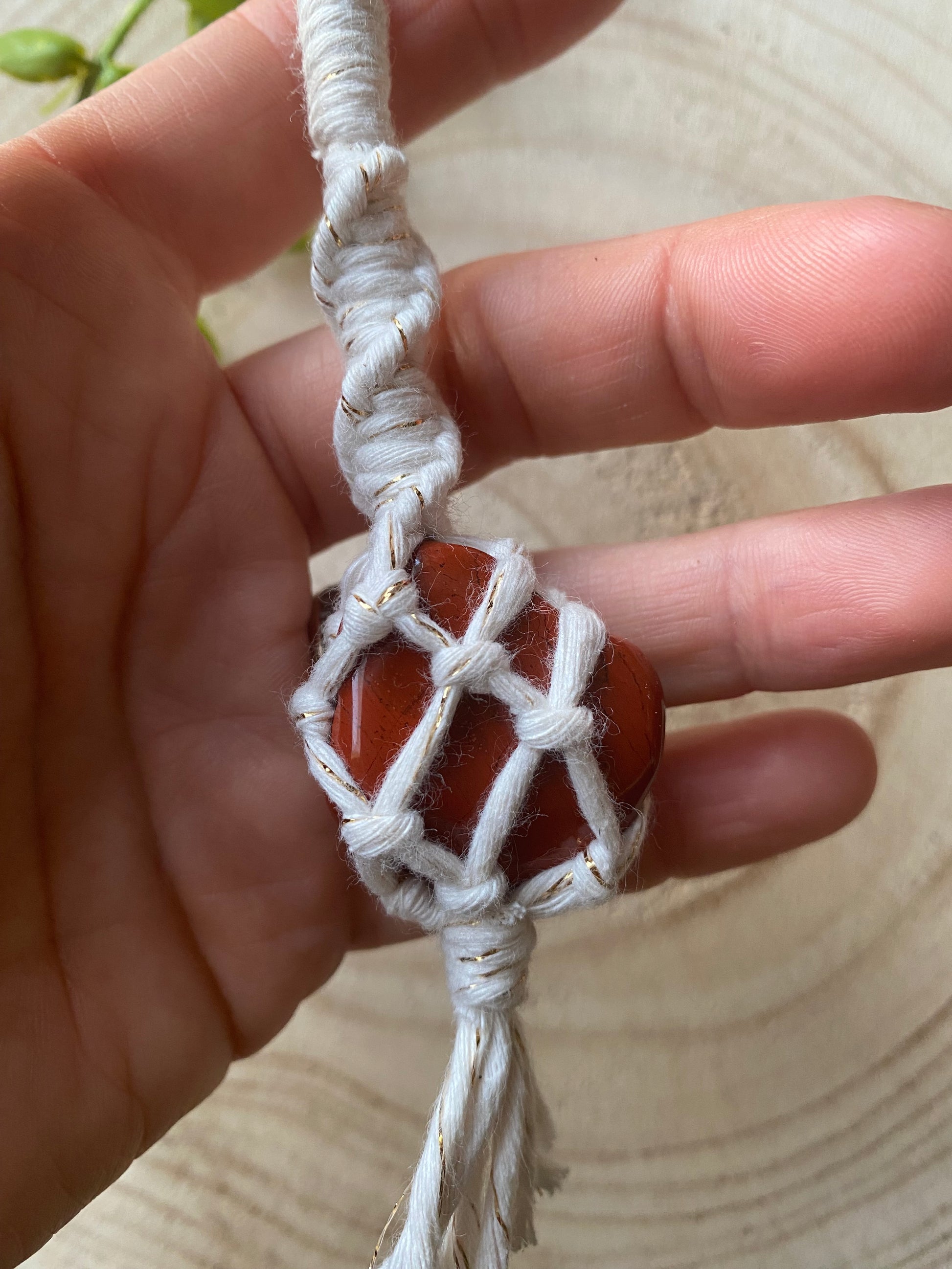 A hand holding a handmade macrame gemstone keyring, made with natural coloured cotton yarn wrapped around a red jasper gemstone.
