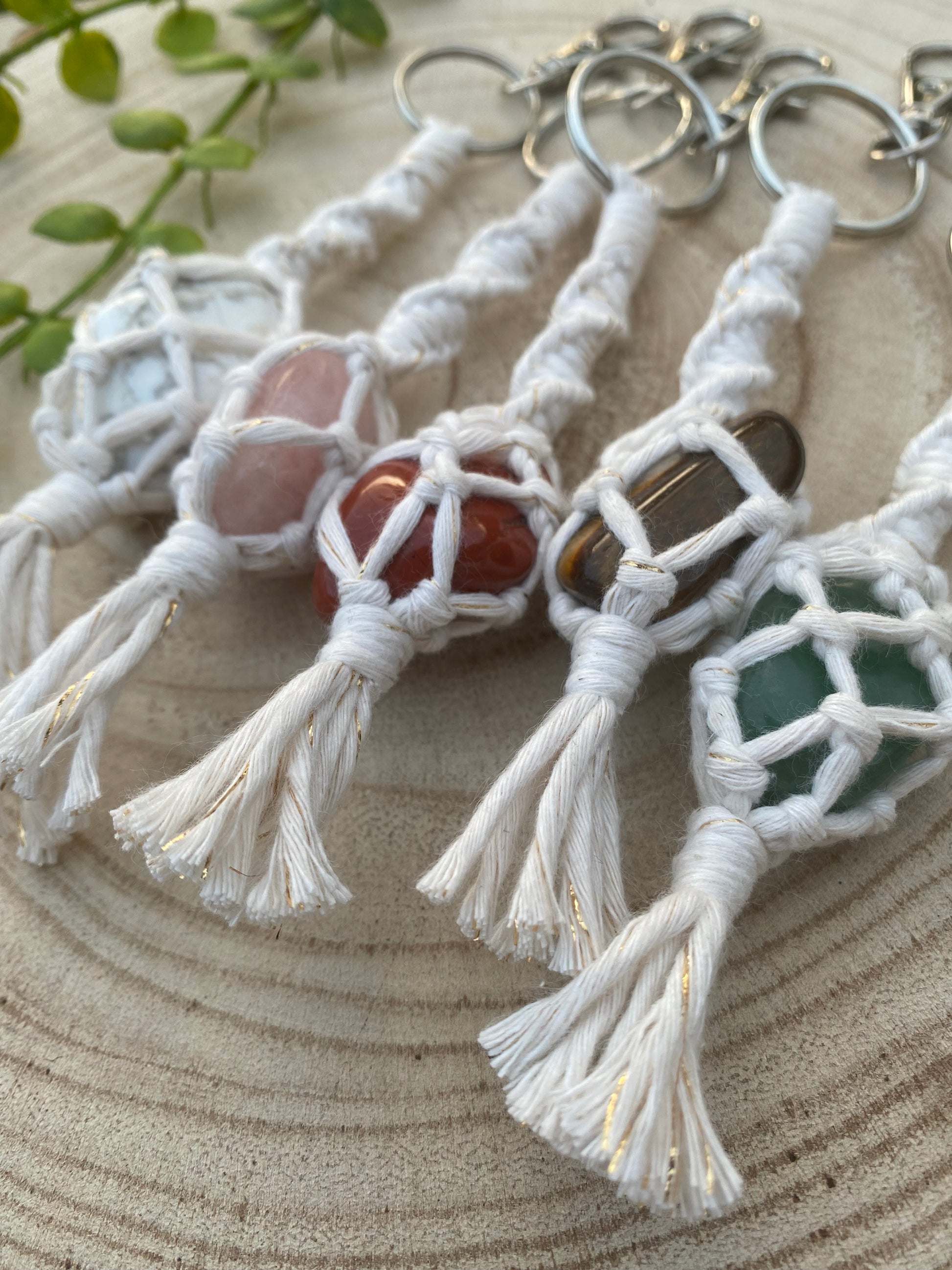 A close up image of 5 handmade macrame gemstone keyrings, made with natural coloured cotton yarn and metal split ring clasps, each with a different gemstone held in the macrame knots. 