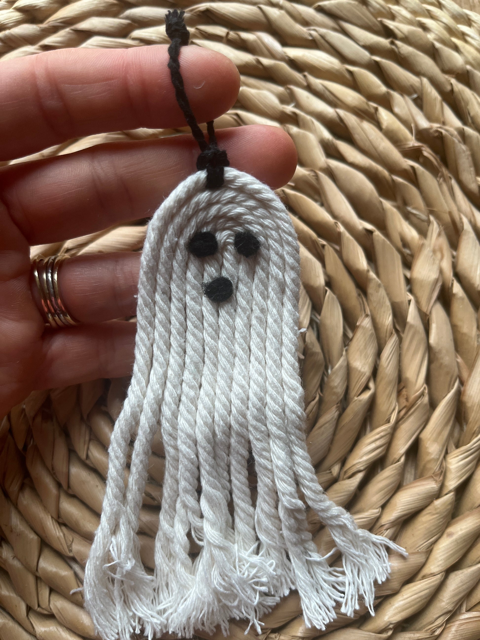 White tassel ghost held by a hand against a woven mat background