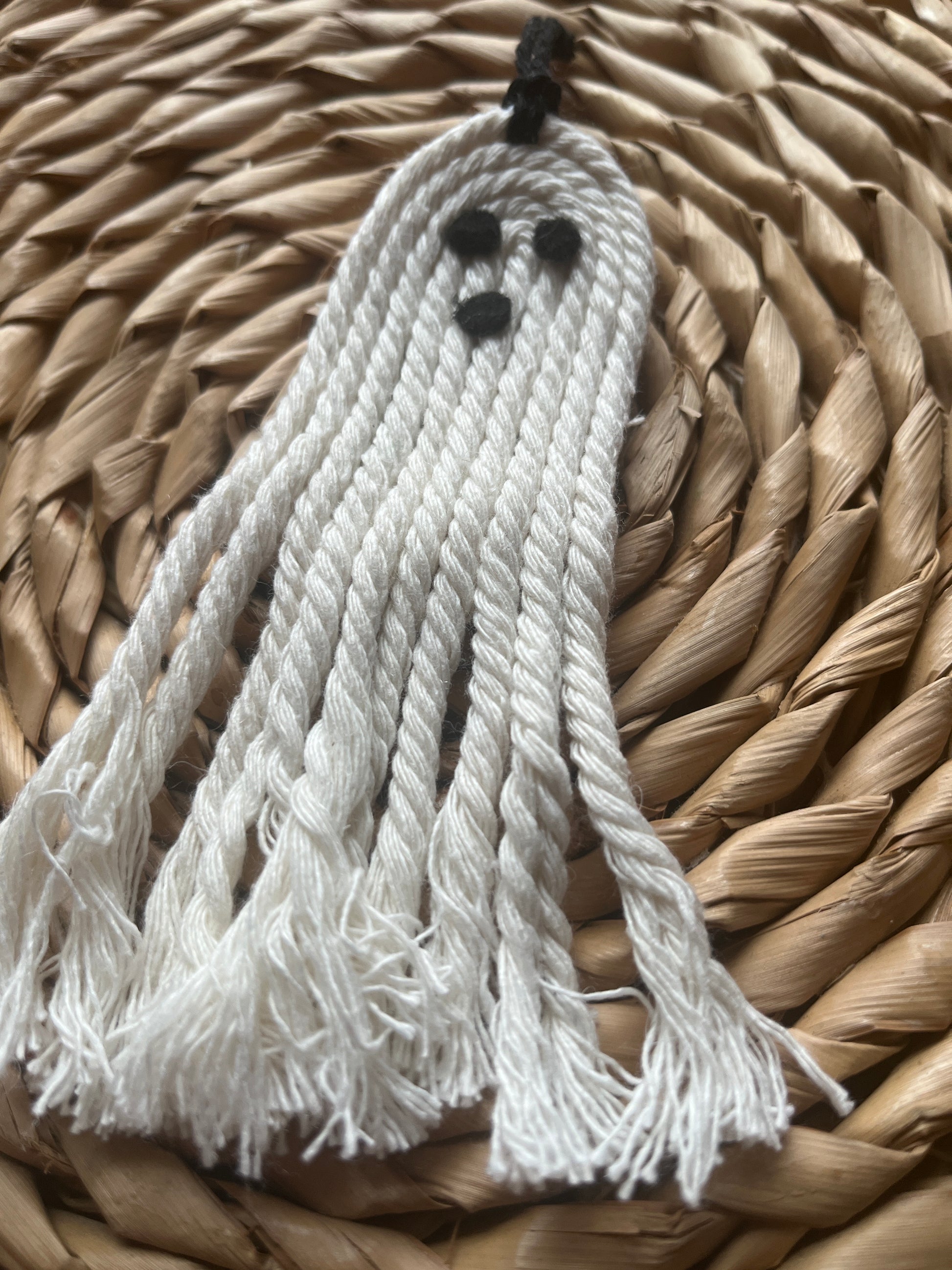 White tassel ghost with black felt face details, on a woven surface