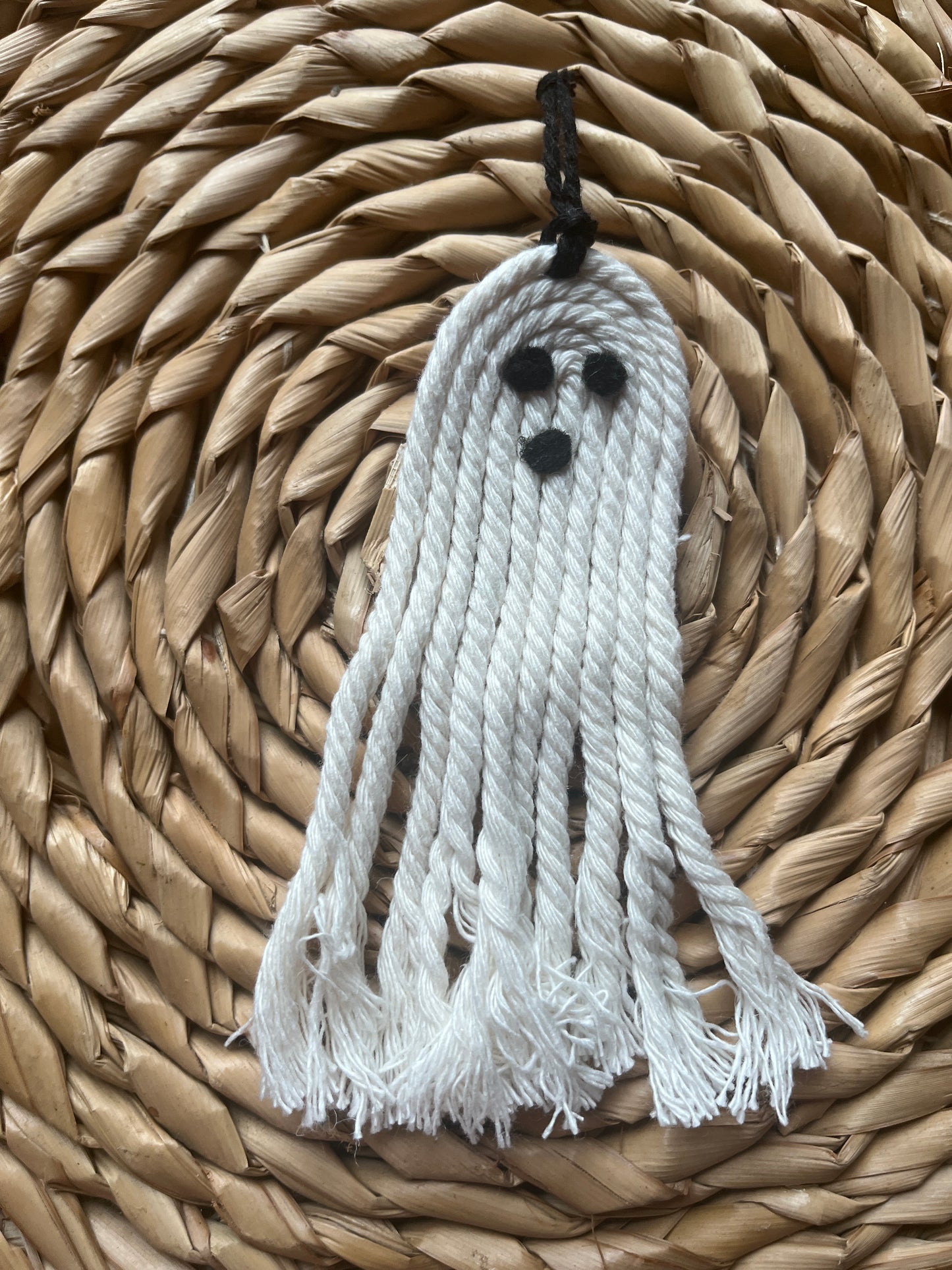 White ghost-shaped tassel with black eyes on a woven mat