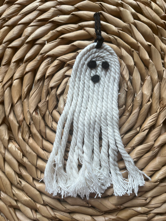 White ghost-shaped tassel with black eyes on a woven mat