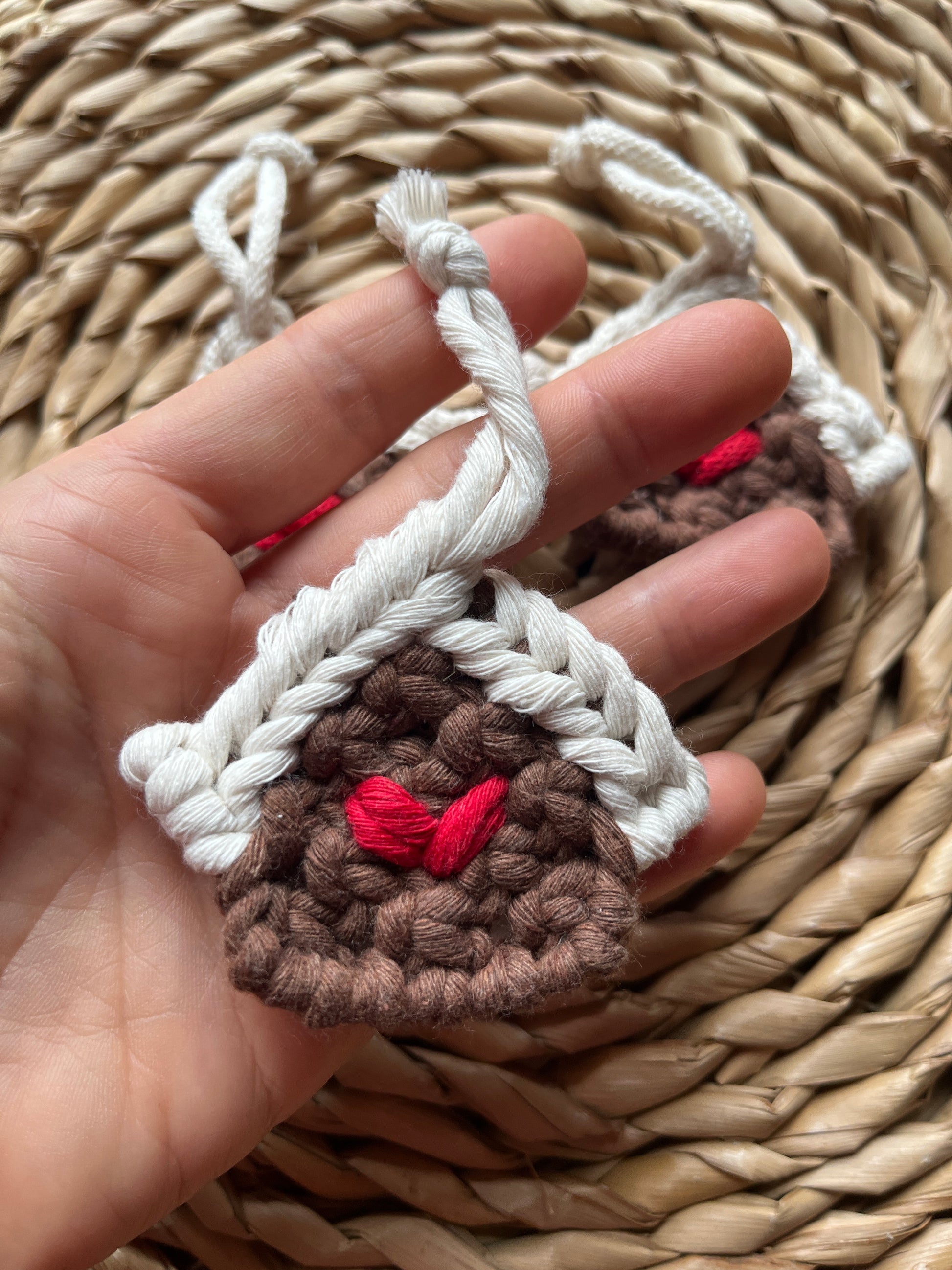 Hand holding a small macrame gingerbread house decoration against a woven background.