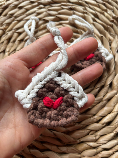 Hand holding a small macrame gingerbread house decoration against a woven background.