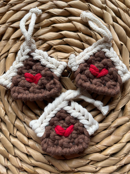 Three handmade macrame gingerbread house decorations on a woven surface