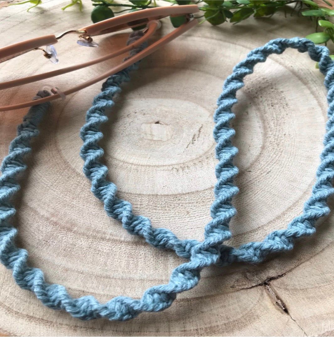 Pink sunglasses with a duck egg blue spiral knotted chain, on a wooden surface.