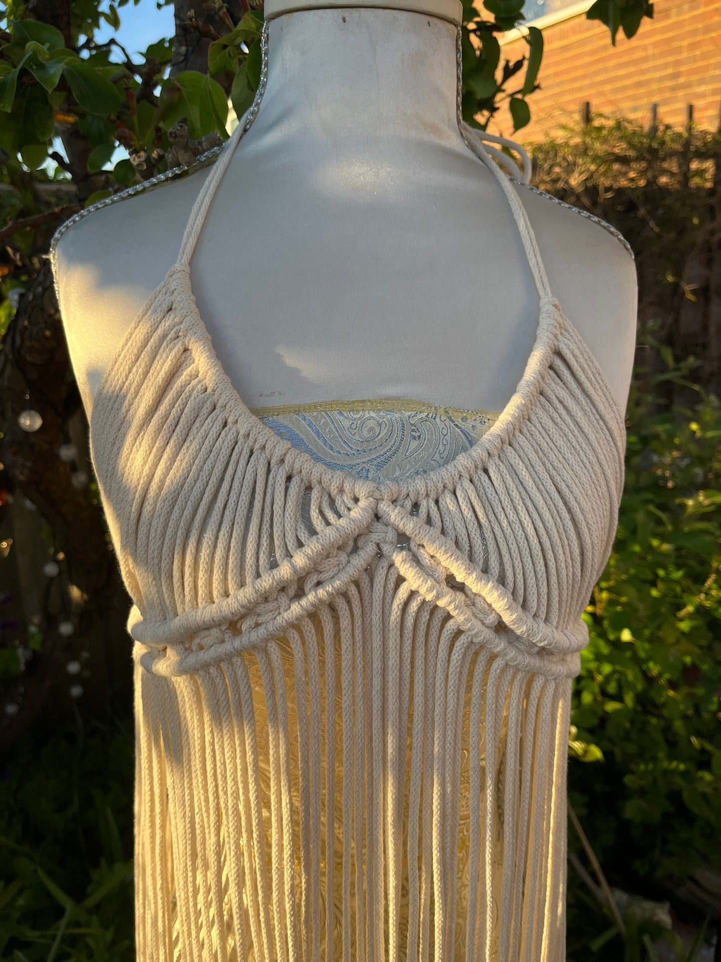Close up of a natural macrame boho goddess dress coverup with halter neck displayed on a mannequin outdoors.