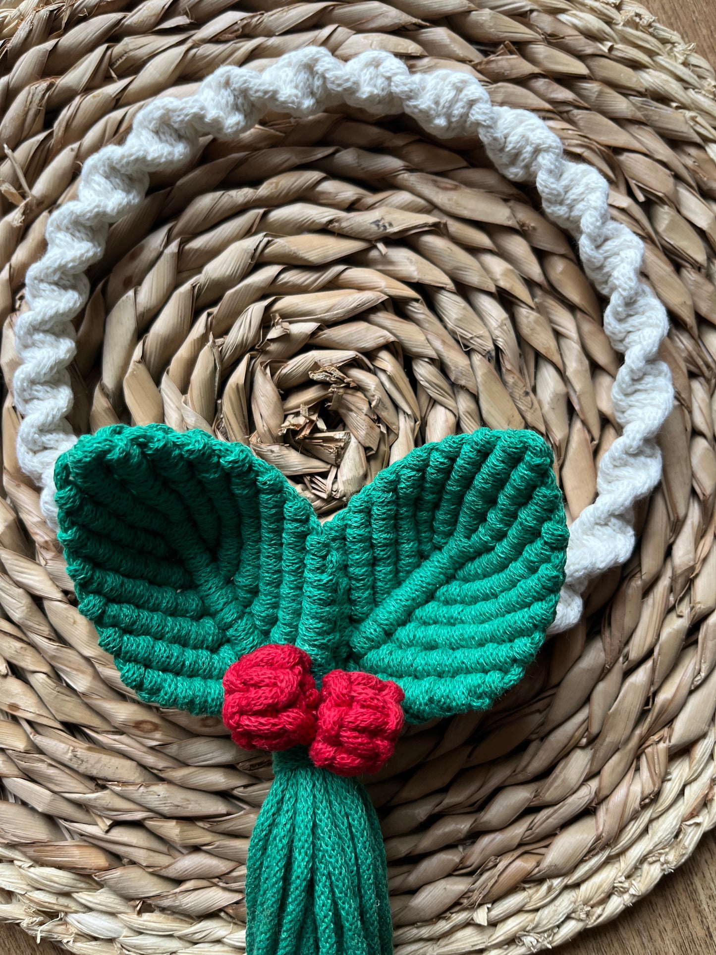Knotted circular macrame wreath with green leaves and red berries o a woven mat