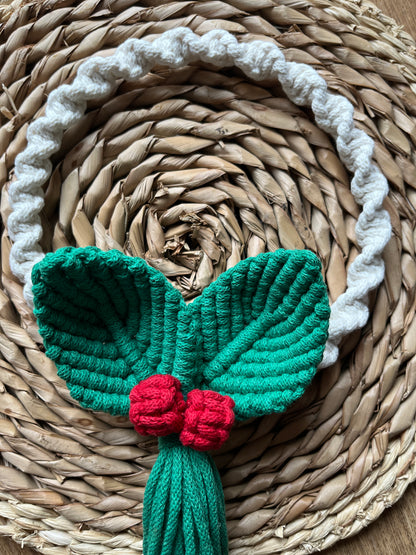 Knotted circular macrame wreath with green leaves and red berries o a woven mat