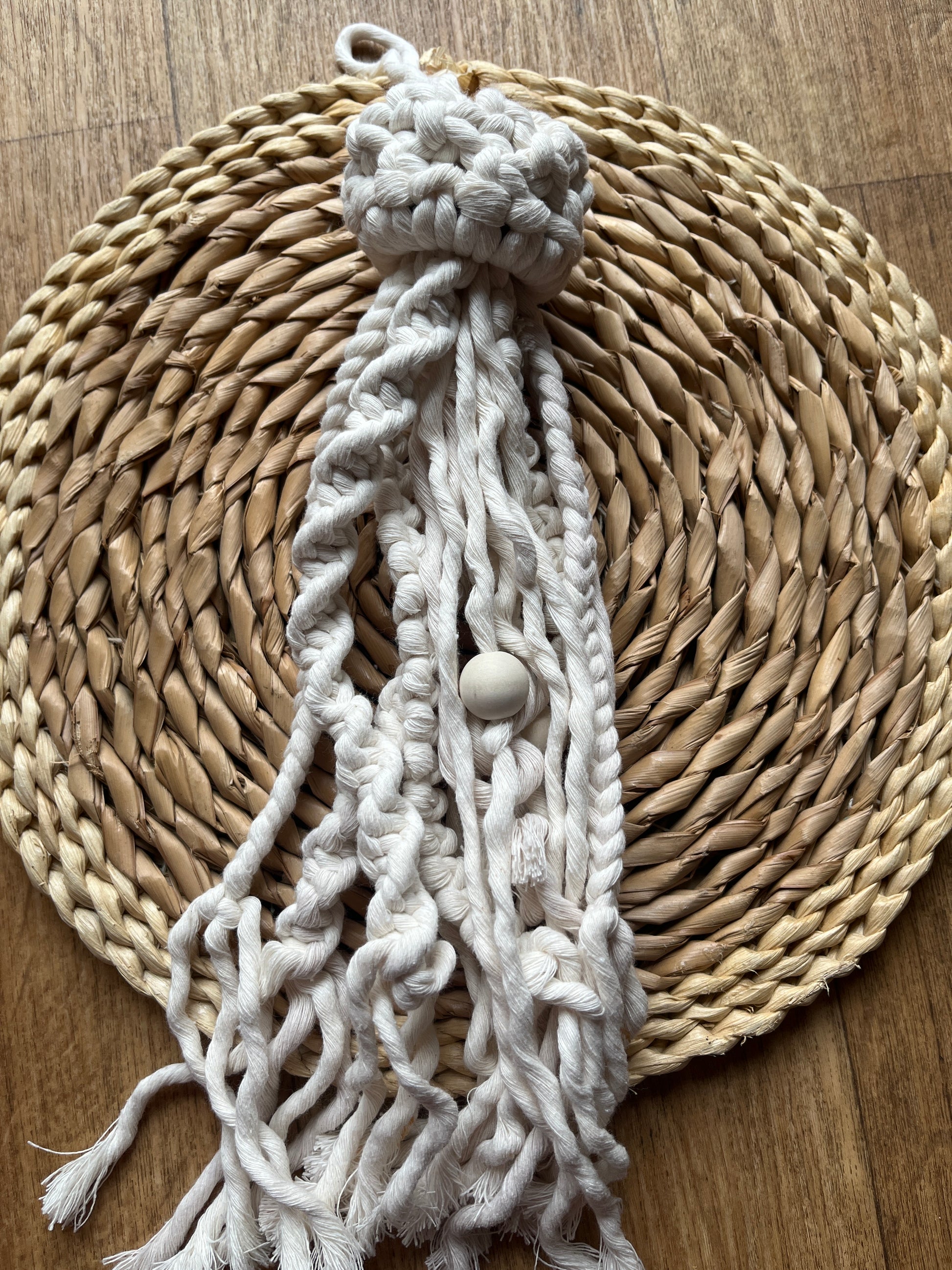 Macrame wall hanging in the shape of a jellyfish on a woven mat