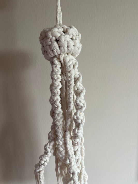 Close-up of a knotted white macrame jellyfish on a plain background