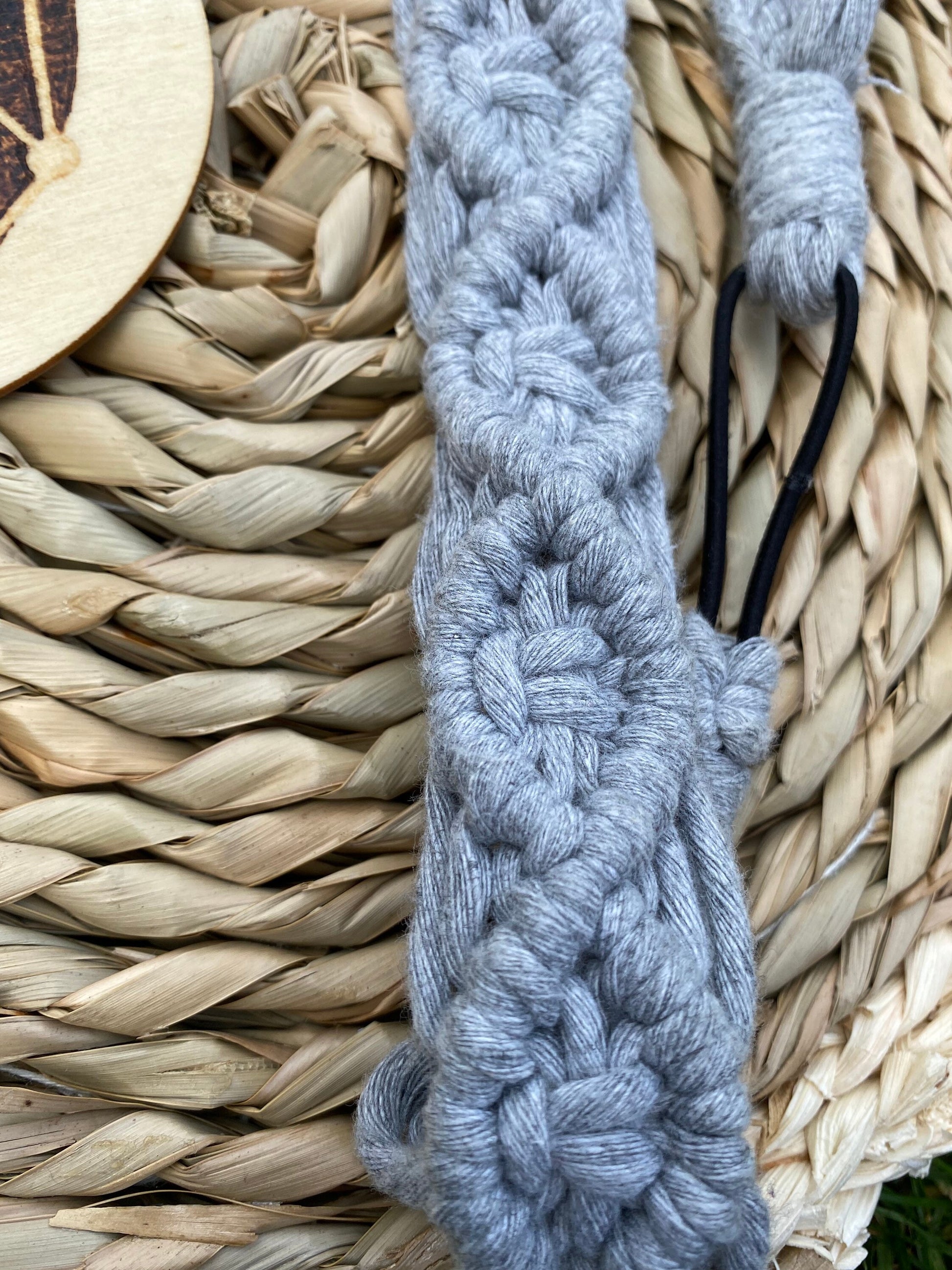 Close up of a grey knotted headband made from recycled cotton cord with an elastic finish, displayed on a woven placemat.