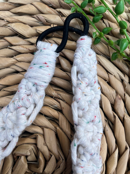 Close up of an infinite knot pattern on a macrame headband made from recycled cotton cord with an elastic finish, displayed on a woven placemat with green plant vines.