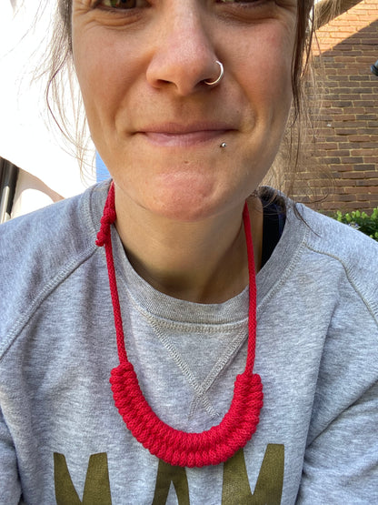 Person smiling at the camera, wearing a grey sweatshirt with a red necklace, outdoors.